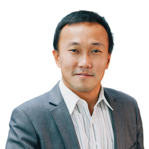 A black haired haired Asian man in a white oxford shirt and gray blazer smiling.