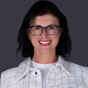 Dark haired woman wearing glasses, smiling at the camera wearing a white plaid jacket and a white t-shirt.