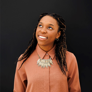 A black woman smiling and looking up in an orange shirt.